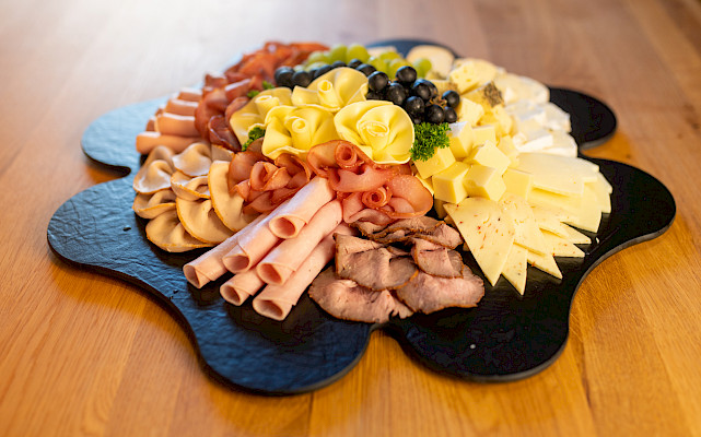 Das Bild zeigt eine Wurst-und Käseblatte auf einem Brett mit der Form eines Kleeblattes.