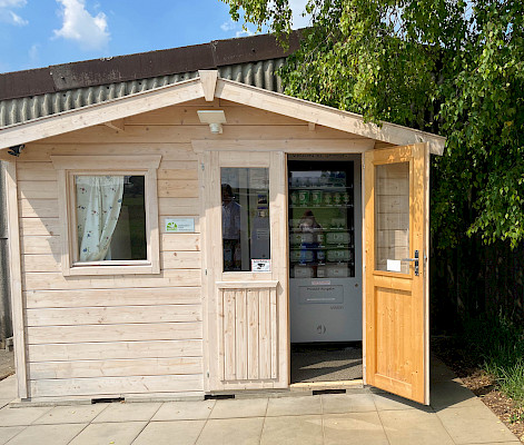 Das Bild zeigt eine Holzhütte, bei welcher die Türe offen steht und man so den darin stehenden Automaten erblicken kann.
